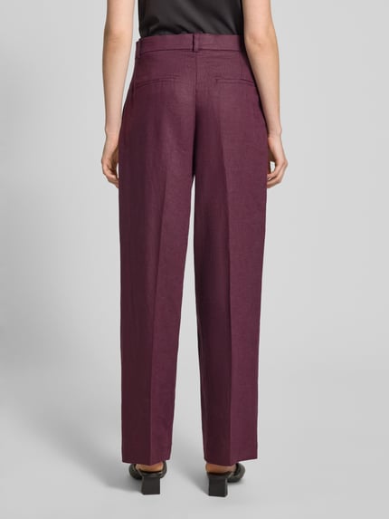 Frauenmodel trägt Straight Fit Leinenhose mit Bügelfalten Modell 'Tempoli' von Mango in Dunkellila, Reine Leinen, Ganzkörperansicht Rückansicht.