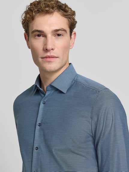 Männermodel trägt Slim Fit Businesshemd mit Kentkragen von OLYMP, einfarbig mit feinem Webstruktur-Muster, Nahaufnahme Oberkörper.