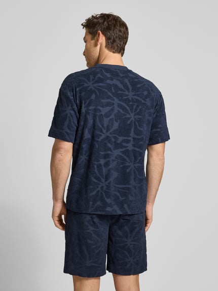 Männermodel trägt Regular Fit T-Shirt aus Baumwoll-Mix Modell 'TE_FLOWER' von BOSS Orange mit Allover-Muster in Dunkelblau, Frottee-Struktur, Ganzkörperansicht Rückansicht.