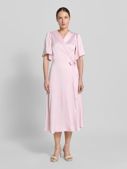 Modelka kobieca ma na sobie różowe, satynowe Midikleid in Wickel-Optik Modell 'VIENNA RAVENNA' od Vila, krój dopasowany w talii, dekolt V, długość tyłu w rozmiarze 36: 125 cm, szerokość w rozmiarze 36: 50 cm, długość rękawa w rozmiarze 36: 30 cm, widok całej sylwetki z przodu.