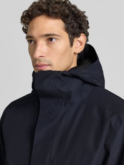 Männermodel trägt Regular Fit Jacke mit Kapuze Modell 'Adam' von Didriksons in Dunkelblau, glatte Struktur, Nahaufnahme Oberkörper. Herren Jacke, Kapuze, Eingrifftaschen, Rückenlänge 79 cm, Schulterbreite 46 cm, Brustweite 58 cm, Ärmellänge 73 cm.