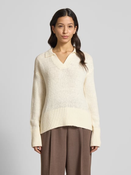 Frauenmodel trägt Strickpullover mit V-Ausschnitt von Fynch-Hatton in Creme, Baumwoll-Mix mit Stretch-Anteil, lockerer Schnitt, Resort-Kragen, gerippte Abschlüsse, braune Hose, Ganzkörperansicht von vorne.