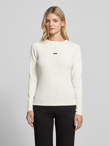 Modelka kobieta nosi Slim Fit Longsleeve aus elastischem Baumwoll-Mix von Karo Kauer, kremowy kolor, krótka listwa guzikowa, label patch, krój slim fit, elastyczna mieszanka bawełny, długość pleców w rozmiarze S: 61 cm, Ganzkörperansicht von vorne.