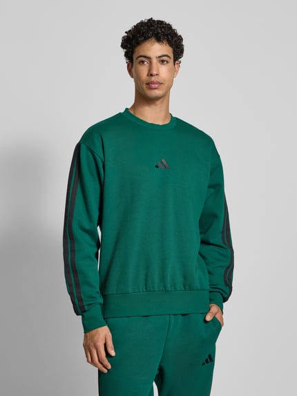 Männermodel trägt Sweatshirt mit Logo und Rundhalsausschnitt von adidas Sportswear in Grün, Baumwoll-Viskose-Mix, Relaxed-Fit, Nahaufnahme Oberkörper.
