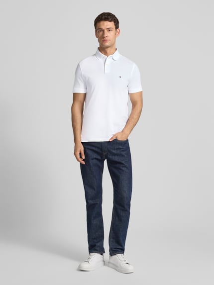 Männermodel trägt Regular Fit Poloshirt mit Logo-Stitching von Tommy Hilfiger aus Baumwoll-Elasthan-Mix, Ganzkörperansicht von vorne.