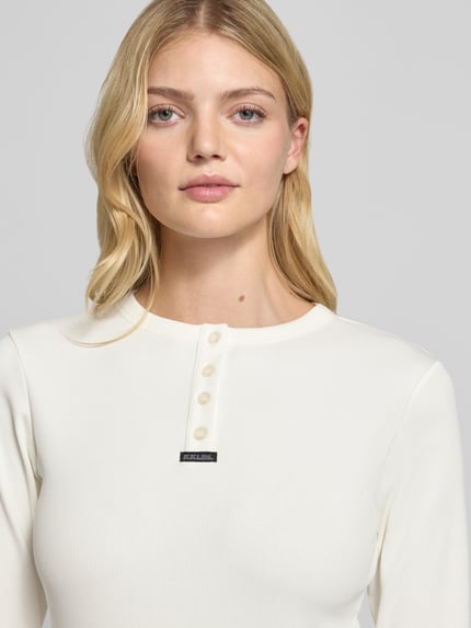 Modelka kobieca nosi Slim Fit Longsleeve aus elastischem Baumwoll-Mix von Karo Kauer, krój slim fit, krótka listwa guzikowa, łatka z logo, elastyczna bawełna, długość pleców w rozmiarze S: 61 cm, kremowy kolor, prosta faktura, zbliżenie na górną część ciała.