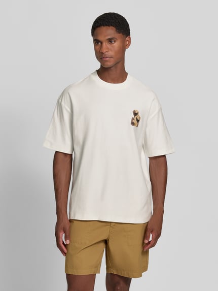 Männermodel trägt Regular Fit T-Shirt aus reiner Baumwolle Modell 'Detzi' von HUGO, cremeweiß, dezente Verzierung, lockere Form, Herren T-Shirt, Ganzkörperansicht von vorne.