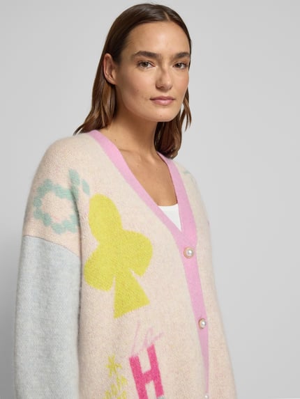 Frauenmodel trägt Cardigan aus Woll-Mix mit V-Ausschnitt und Knopfleiste von Herzensangelegenheit, pastellige Farben, Nahaufnahme Oberkörper.