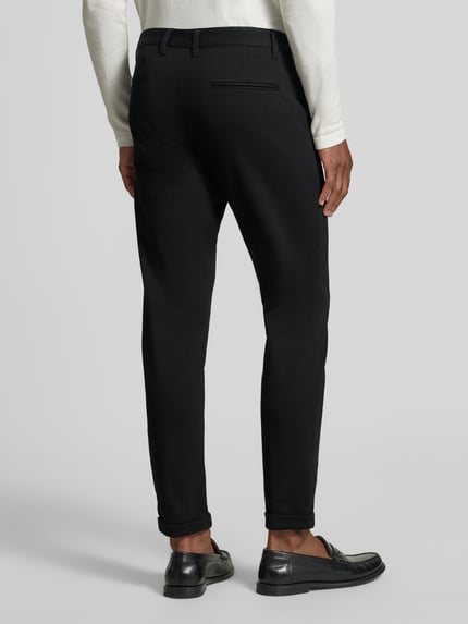 Männermodel trägt Slim Fit Stoffhose mit umgeschlagenen Hosenbeinen von Lindbergh in Schwarz, elastischer Material-Mix, Ganzkörperansicht Rückansicht.