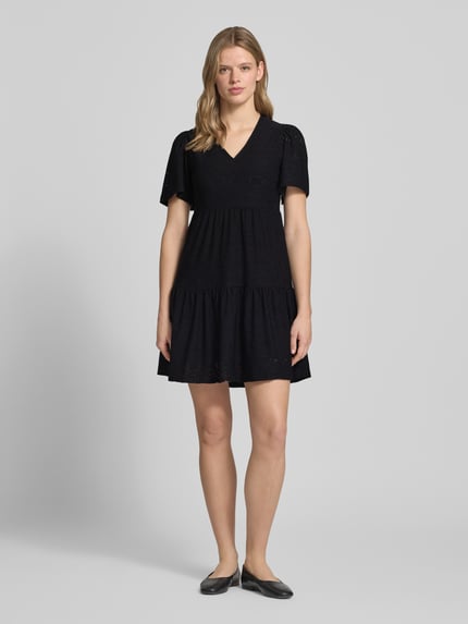 Frauenmodel trägt Mini-Freizeitkleid mit Lochstickmuster Modell 'SMILLA LIFE' von Only, unifarben, Regular Fit, V-Ausschnitt, Mini-Länge, Trennnähte, kurzarm, Ganzkörperansicht von vorne.