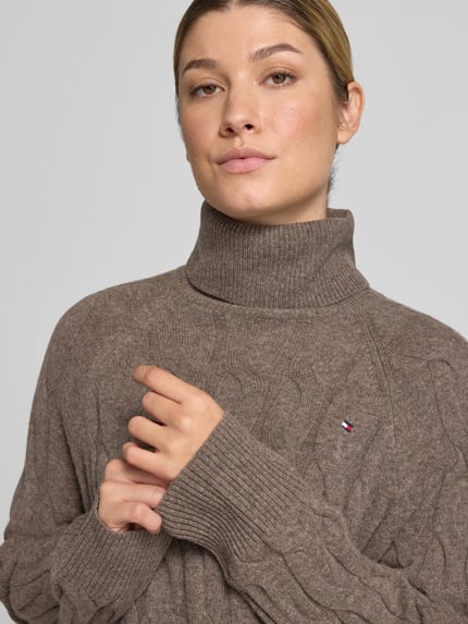 Kobieta nosi Relaxed Fit Rollkragenpullover aus reiner Wolle od Tommy Hilfiger, brązowy, widoczne faktury dzianiny, zbliżenie na górę ciała.
