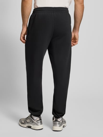 Männermodel trägt Sweatpants mit Label-Stitching von KARL KANI in Schwarz, Baumwoll-Mix, Regular-Fit, elastischer Bund, Ganzkörperansicht Rückansicht.