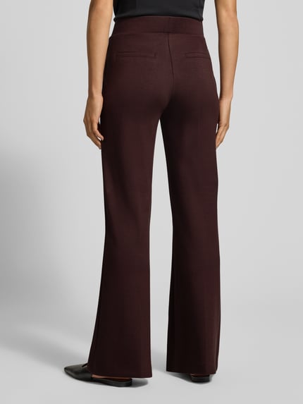Frauenmodel trägt Flared Cut Hose mit elastischem Bund von Christian Berg Woman in Dunkelbraun, glatte Textur, Gesäßtaschen, Material-Mix mit Viskose-Anteil, Ganzkörperansicht Rückansicht.