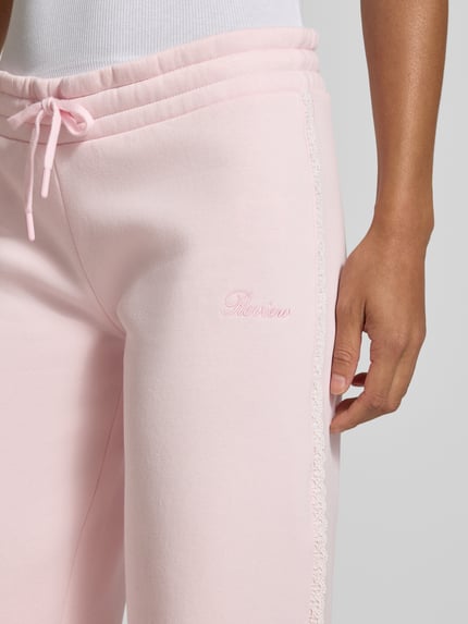 Frauenmodel trägt Wide Fit Sweatpants aus Baumwoll-Mix von REVIEW in Rosa mit Bordüre, Label-Stitching, Nahaufnahme Oberkörper.