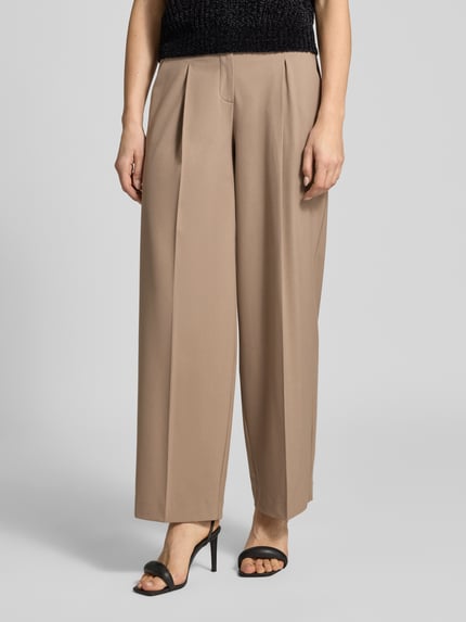 Frauenmodel trägt Stoffhose mit Gesäßtasche Modell 'Maiga' von Opus aus Material-Mix mit Viskose-Anteil, lockerem Schnitt, Bundfalten, französischen Eingrifftaschen, Knopf- und Reißverschluss, Bundweite bei Größe 36: 38 cm, Innenbeinlänge 77 cm, helle Beige-Töne, glatte Textur, Nahaufnahme Oberkörper.