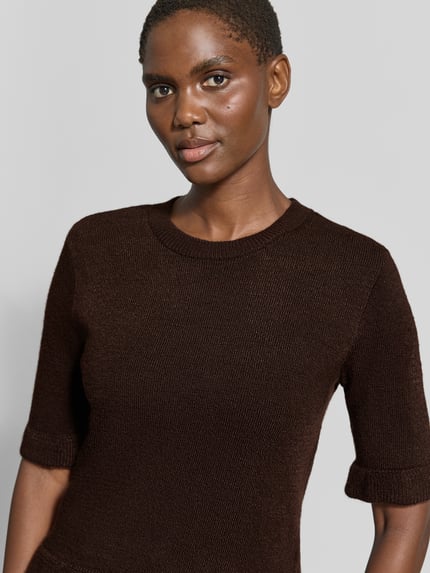 Frauenmodel trägt Longsleeve mit Viskose-Anteil von MORE & MORE, braune Strick-Optik, körpernah, Rüschenbesatz, Nahaufnahme Oberkörper.