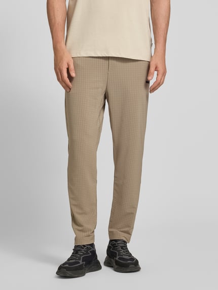 Männermodel trägt Tapered Fit Hose mit Waffelstrukturmuster Modell 'TERRACE' von BOSS Green in Beige, Seiten- und Vorderansicht, Nahaufnahme Unterkörper. Moderne Herren Hose mit Allover-Waffelmuster, elastischem Bund mit Tunnelzug und seitlichen Eingrifftaschen.