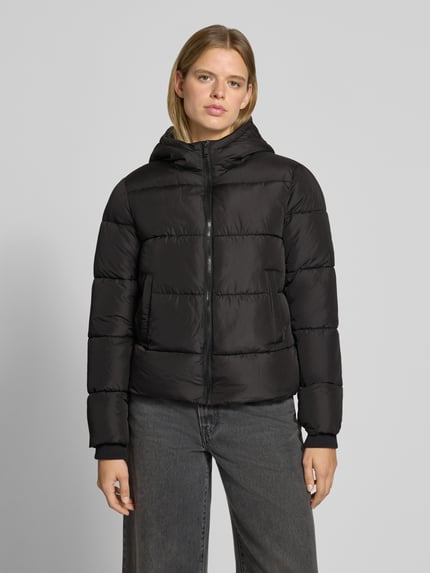 Frauenmodel trägt schwarze Steppjacke mit Kapuze von PIECES, glatte Textur, dezente Nähte, lockere Passform, Ganzkörperansicht von vorne.