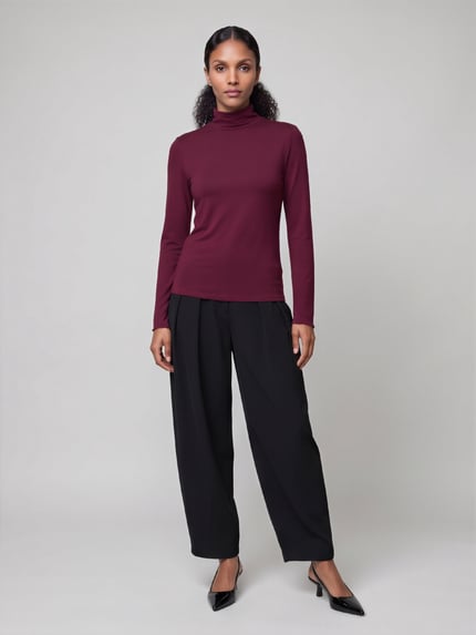 Frauenmodel trägt ein bordeauxfarbenes Langarmshirt aus Wolle mit Rollkragen von S. OLIVER BLACK LABEL, kombiniert mit schwarzer Hose, Lyocell-Woll-Mix, unifarbene Optik, Ganzkörperansicht von vorne.
