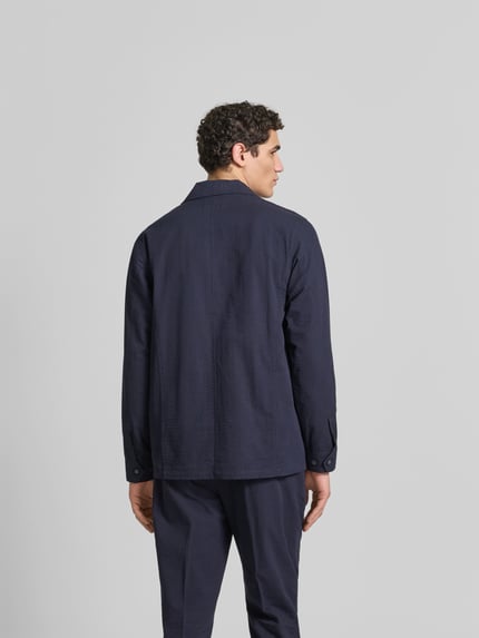 Męski model nosi Relaxed Fit Hemdjacke aus Baumwolle od Officine Générale, kolor granatowy, wyraźna faktura, kołnierz z połami, listwa guzikowa, nakładane kieszenie, długość tyłu w rozmiarze M: 74 cm, widok całej sylwetki z tyłu.