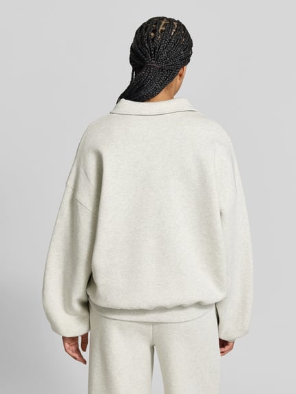 Frauenmodel trägt Oversized Troyer mit Label-Patch von ROTATE aus reiner Baumwolle, hellgraue Farbe, weiche Textur, elastische Abschlüsse, Rückenlänge 65 cm, Ganzkörperansicht Rückansicht.