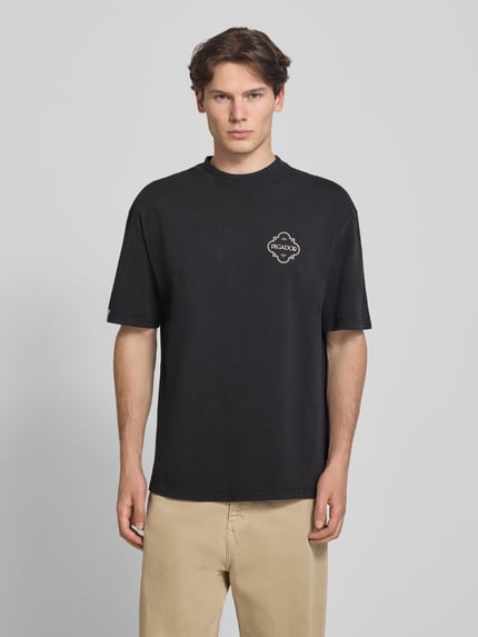 Mannelijk model draagt Oversized T-shirt met labelprint model 'Paide' van Pegador in zwart, puur katoen, ronde hals, heren, frontaal, volledige lichaamsopname. Ruglengte bij maat M: 70 cm.