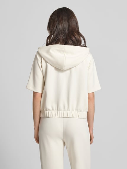 Frauenmodel trägt Sweatjacke mit Halbarm Modell 'Therese' von JOOP! in Creme mit Kapuze, Elastischer-Material-Mix, Gerader-Schnitt, Elastischer Bund, Rückansicht.