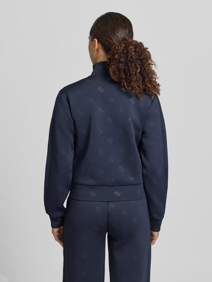 Kobiece modelka nosi Sweatjacke mit Logo-Muster Modell 'CALISTA' od Guess Activewear, materiał z domieszką stretchu, krój regular fit, kolor granatowy, widoczne kieszenie i stójka, widoczne logo, tekstura gładka, widok całej sylwetki z tyłu