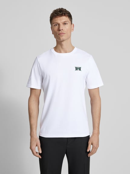 Männermodel trägt Regular Fit T-Shirt mit Logo-Print Modell 'Bobby' von Wood Wood aus weißer Baumwolle, Rundhalsausschnitt, Ganzkörperansicht von vorne.