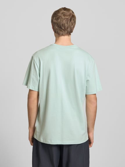 Männermodel trägt T-Shirt mit Logo-Stitching von The North Face in Mintgrün, Baumwolle, gerader Schnitt, Rückenansicht, Ganzkörperansicht Rückansicht.