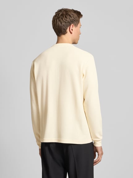 Männermodel trägt Regular Fit Pullover mit Knopfleiste Modell 'Kilano' von Drykorn aus Baumwoll-Mix, cremefarben mit Strukturmuster, Ganzkörperansicht Rückansicht.