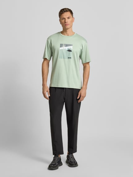 Männermodel trägt Relaxed Fit T-Shirt aus reiner Baumwolle Modell 'JOIN' von BOSS Green in lichtgroen met motiefprint, unifarben, label stitching, ronde hals, korte mouwen, Ganzkörperansicht von vorne.