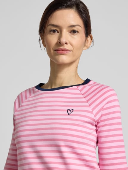 Frauenmodel trägt Shaped Fit T-Shirt aus reiner Baumwolle von Tom Tailor Denim, pink-weiß gestreift, Rundhals, Feinripp, Nahaufnahme Oberkörper.