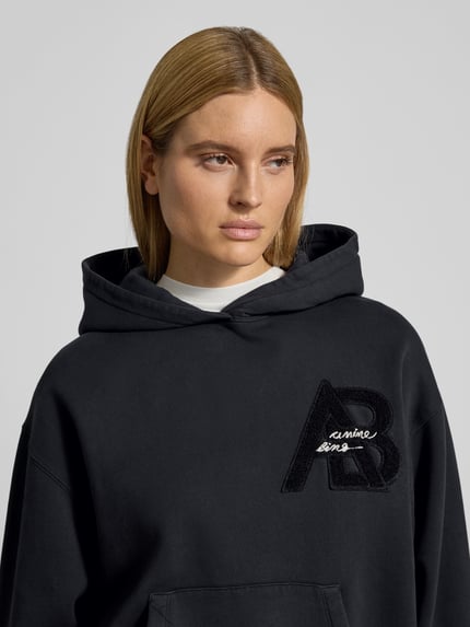 Frauenmodel trägt Regular Fit Hoodie mit Logo-Detail von Anine Bing, reine Baumwolle, Logo-Detail, Känguru-Tasche, elastische Abschlüsse, Nahaufnahme Oberkörper.