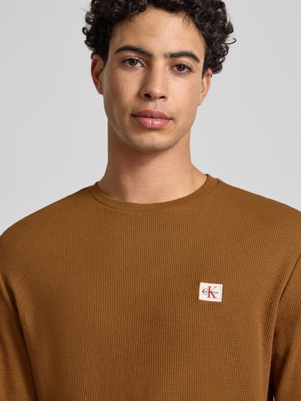 Männermodel trägt Slim Fit Longsleeve mit Logo-Patch Modell 'Waffle' von Calvin Klein Jeans, braun, Piqué-Struktur, Nahaufnahme Oberkörper.