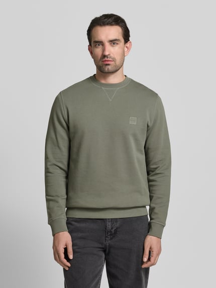 Männermodel trägt Relaxed Fit Sweatshirt aus reiner Baumwolle Modell 'WESTART' von BOSS Orange, unifarben, Label Patch, Rundhals, Ganzkörperansicht von vorne.