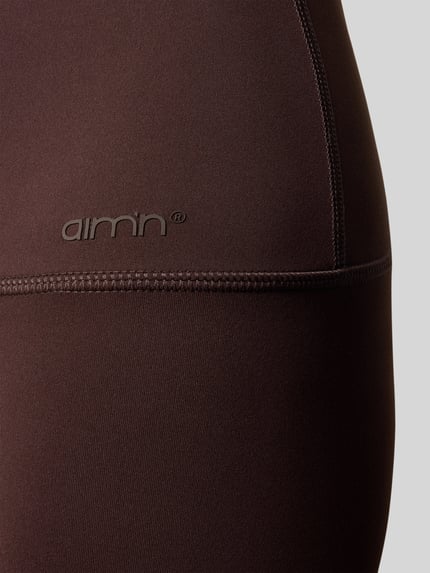 Frauenmodel trägt Leggings mit elastischem Bund Modell 'Sense' von aim'n, dunkelbrauner Stoff mit glatter Textur, Nahaufnahme Oberschenkel.