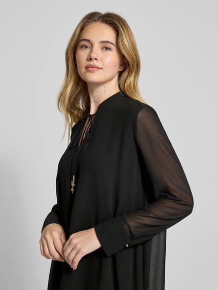 Vrouwenmodel draagt knielang, zwart JOOP! 'Knielanges Kleid mit Stehkragen Modell Delilah', losvallend, semi-transparant, lange mouwen, Nahaufnahme bovenlichaam.
