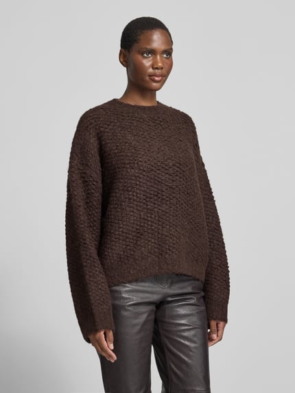 Frauenmodel trägt Pullover mit asymmetrischem Saum Modell 'CORSETTA' von black palms, unifarben, Strickoptik, Struktur, Rundhals, langarm, gerippte Abschlüsse, Ganzkörperansicht von vorne.