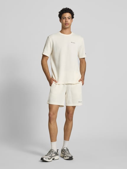 Männermodel trägt Shorts mit Strukturmuster und elastischem Bund von CHAMPION in Creme, Label-Stitching, Baumwoll-Mix, Ganzkörperansicht von vorne.