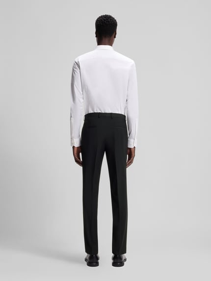 Mężczyzna model nosi Slim Fit Anzughose aus Woll-Mix Modell 'HESTEN' od HUGO, czarny melanż, gładki materiał, widok całej sylwetki z tyłu, krój slim fit, szerokość w rozmiarze 50: 45 cm, długość nogawki wewnętrznej: 79,5 cm, kieszenie boczne i tylne, zapięcie na hak i ukryty zamek, szlufki na pasek, spodnie z kantem