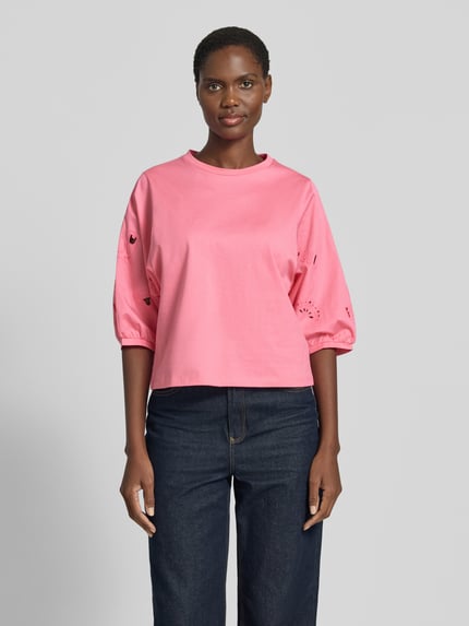 Kobiece modelka nosi t-shirt z rękawem o dł. 3/4 i haftem angielskim od Marc Cain, bawełna, krój regular fit, okrągły dekolt, długość tyłu w rozmiarze 36: 52 cm, różowy kolor, przód, całopostaciowy widok.
