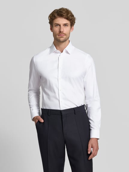Männermodel trägt weißes Slim Fit Businesshemd aus reiner Baumwolle von Jake*s, glatte Textur, dunkle Hose, Ganzkörperansicht von vorne.