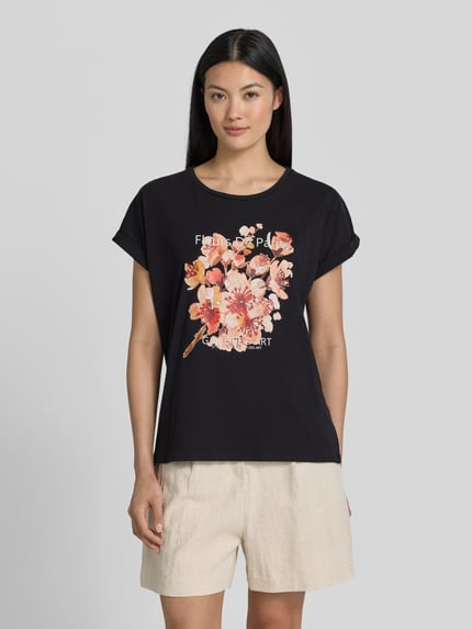 Vrouwenmodel draagt T-shirt met motiefprint model 'RINA' van Soyaconcept, mix van katoen en elastaan, regular fit, dames, ronde hals, mouwen met omslag, ruglengte bij maat S 61 cm, zwart met bloemmotiefprint, vooraanzicht van het hele lichaam.