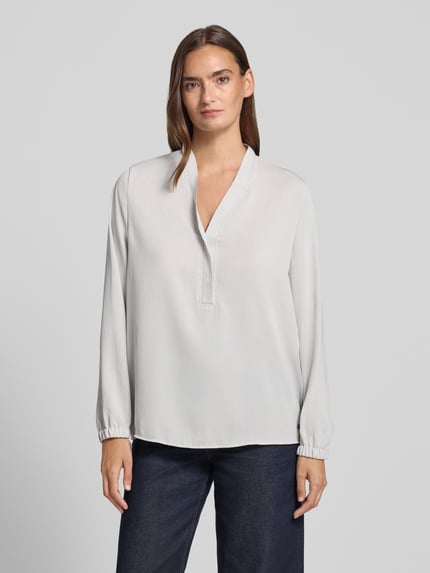 Kobiece model prezentuje Regular Fit Bluse mit V-Ausschnitt von Marc Cain, jasna bluzka o kroju regular fit z dekoltem w serek, detal z logo, długość tyłu w rozmiarze 36: 65 cm, długość rękawów w rozmiarze 36: 59 cm, przód, całkowity widok.