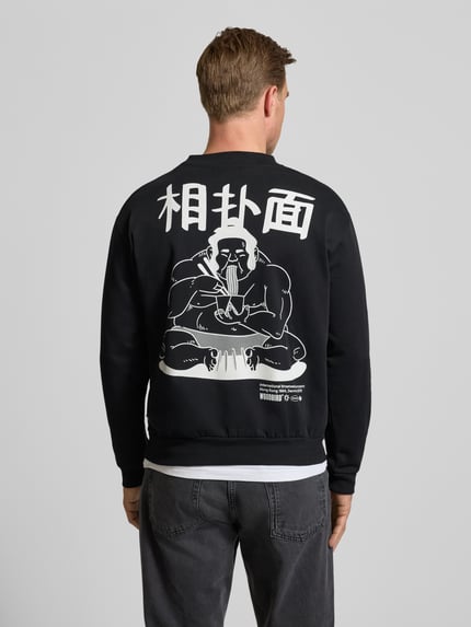 Männermodel trägt Sweatshirt mit Label-Print Modell 'Cane' von WOODBIRD in Schwarz mit Weiß, Bio-Baumwolle, Rückenansicht, Ganzkörperansicht.