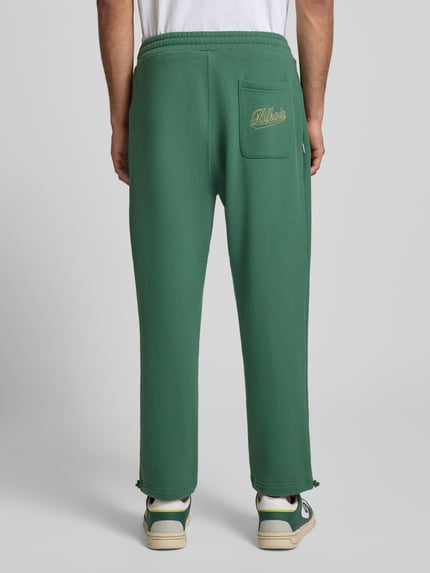Männermodel trägt grüne Regular Fit Sweatpants mit Gesäßtasche Modell 'Source' von BLKVIS aus reiner Baumwolle, 7/8-Länge, Ganzkörperansicht Rückansicht.