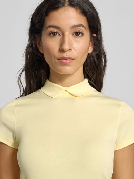 Frauenmodel trägt Slim Fit T-Shirt mit Polokragen von Marc Cain aus Baumwoll-Elasthan-Mix, Label-Detail, Nahaufnahme Oberkörper.