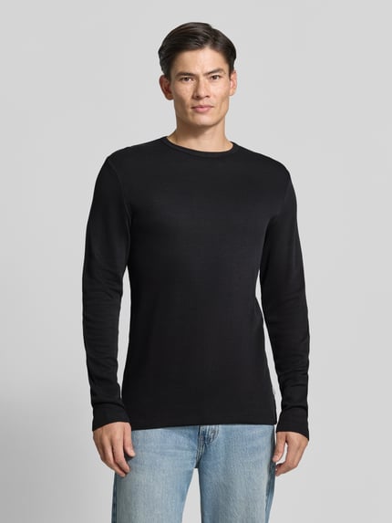 Männermodel trägt Regular Fit Longsleeve aus reiner Baumwolle Modell 'Basic' von Lindbergh in Schwarz, Jeans, Ganzkörperansicht von vorne. Rückenlänge bei Größe M: 73 cm, Rundhalsausschnitt, Herren Longsleeve.