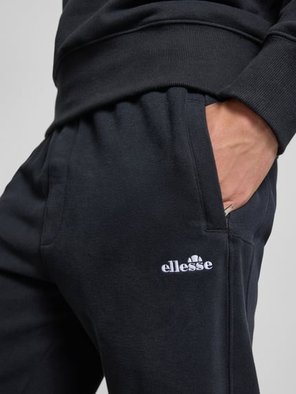 Männermodel trägt Sweatpants mit Logo-Stitching Modell 'ORVINIO' von Ellesse aus Baumwoll-Mix in Schwarz, Nahaufnahme Oberkörper.